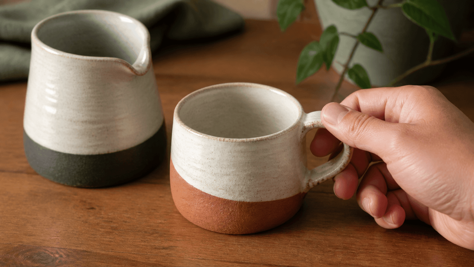 Bàn tay cầm thử quai ly gốm cạnh một bình cà phê nhỏ