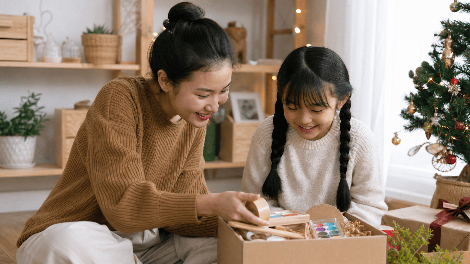 Người lớn cùng bé gái mở hộp quà hoạt động sáng tạo cạnh cây thông nhỏ